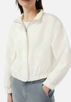 White cropped jacket with textured fabric, high collar, and zip front. Features elastic cuffs and side pockets, paired with gray pants.