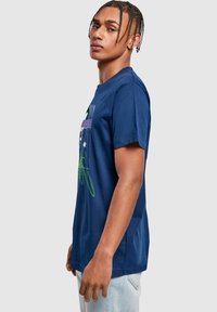 Marineblå bomulds t-shirt med korte ærmer, der har et grafisk print foran i grøn og lilla. Klassisk pasform med rund halsudskæring.