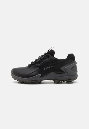 Black athletic shoes with a smooth synthetic upper, textured mesh collar, and rubber outsole featuring molded traction spikes.