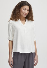 Blusa bianca in lino con colletto alla cinese, patta con bottoni e maniche arrotolate, caratterizzata da una vestibilità morbida e una consistenza delicata.