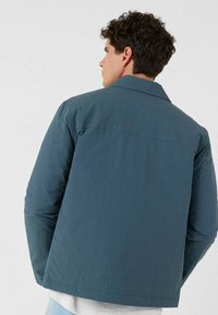 Eine blaue, leichte Jacke mit glatter Textur, ausgestattet mit einem klassischen Kragen und einem geraden Schnitt, von hinten betrachtet.