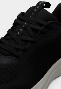 Κοντινή λήψη ενός μαύρου αθλητικού παπουτσιού από δίχτυ με παχιά κορδόνια και λευκή σόλα, που τονίζει το υφασμάτινο υλικό με υφή και τις λεπτομέρειες των βρόχων των κορδονιών.