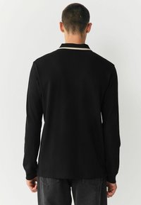 Black long-sleeve shirt with a simple collar, featuring cream accents. Soft material with a smooth texture. Plain design, no patterns or graphics.