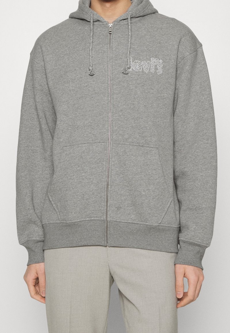 Sweat à capuche zippé gris en tissu doux, avec capuche à cordon, poches kangourou et logo Levi's blanc sur le devant.