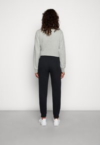 Γκρι κοντό φούτερ με μακριά μανίκια, συνδυασμένο με μαύρα τζόγκερ με ελαστική μέση και λευκά αθλητικά παπούτσια.