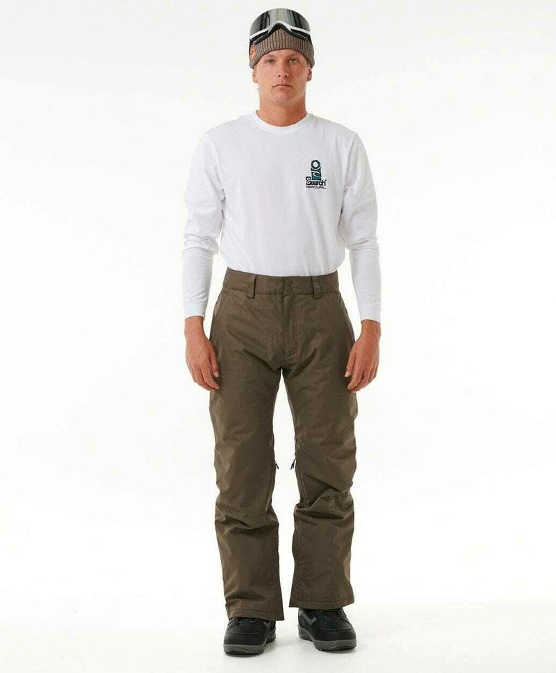 Pantalons de ski marron avec une coupe droite, associés à une chemise à manches longues blanche. La tenue comprend des bottes de neige noires et des lunettes de ski.
