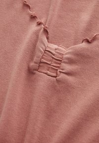 Gros plan sur un tissu rose poussiéreux avec une section élastique texturée et des coutures ondulées décoratives sur un matériau en tricot doux.