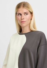 Sweatshirt with a split design, featuring light cream on one side and dark gray on the other. Soft fabric and round neckline.