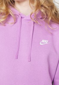 Oversized hoodie i mjukt lila tyg, med en framficka i kängurustil, dragsnören och en vit Nike-logotyp på bröstet.