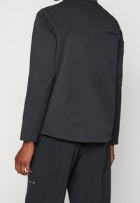 Ciemnoszara kurtka wykonana z gładkiego, fakturowanego materiału z wysokim kołnierzem. Posiada wzór szwów, lekko wydłużony tył i logo na górnej części pleców.