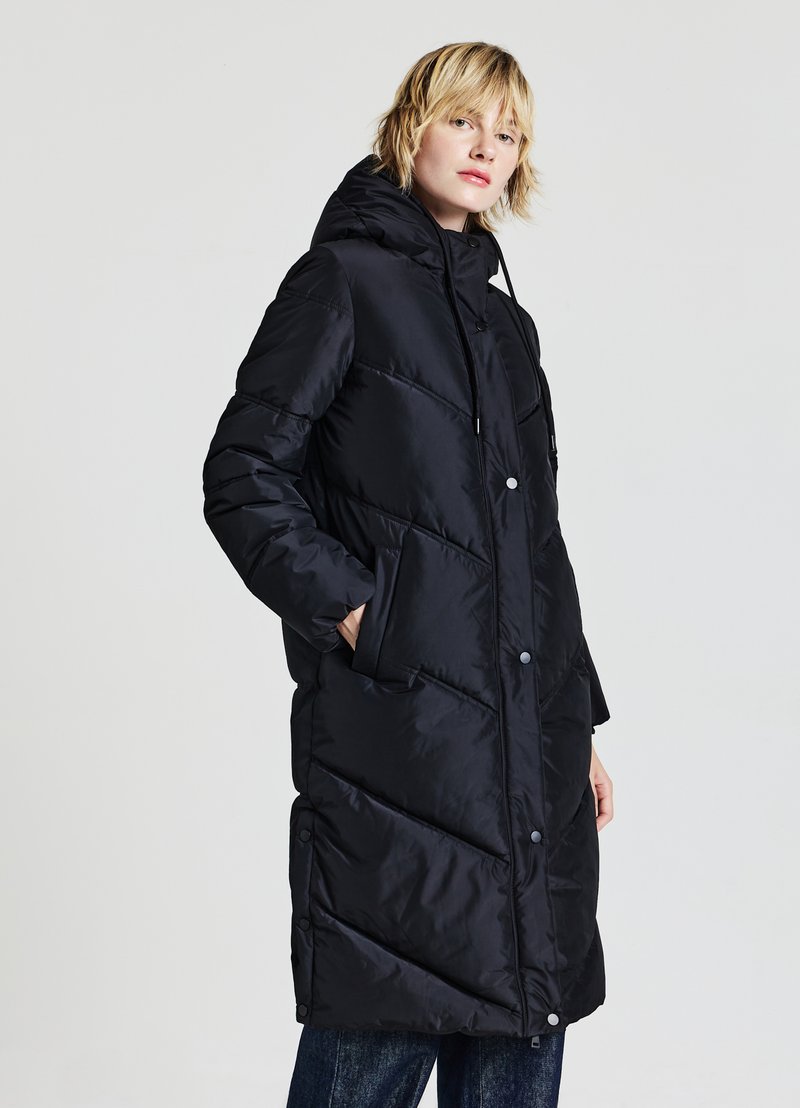 Manteau matelassé noir avec capuche, présentant un motif chevron, des boutons-pression et des poches latérales ; fabriqué en tissu brillant et lisse.