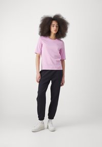 Rosa kortärmad skjorta med rund halsringning, parat med mörkblå joggers och vita sneakers. Slät tygtextur och minimalistisk design.