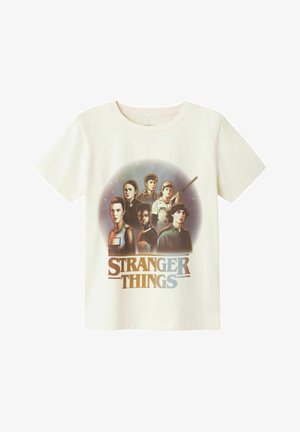 Off-white bomuld t-shirt med grafisk tryk af flere karakterer fra "Stranger Things" samt seriens titel i blå og sort.