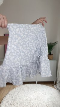 Gaiši zils ziedu kleita ar viļņotu apakšmalu, kas izgatavota no strukturētas auduma. Raksts sastāv no mazām baltām ziediem un ar savilktu jostas detaļu.