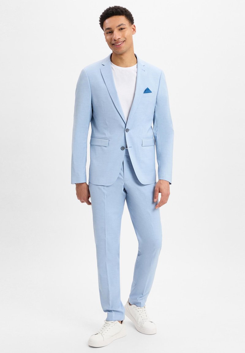 Lichtblauw pak met een op maat gemaakte pasvorm, voorzien van een enkelvoudig gebreid blazer, notched lapels en twee frontzakken. Gecombineerd met een wit T-shirt en witte sneakers.
