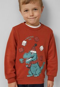 Een roestkleurige sweatshirt met een afbeelding van een T-Rex in een winterhoed en sjaal, omgeven door geïllustreerde cadeaudozen. Gemaakt van katoen, met een ronde hals.