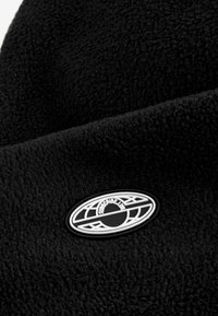 Tissu en polaire noir avec une surface texturée. Présente un patch logo circulaire en noir et blanc, situé sur le côté.