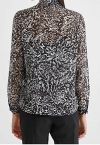 Blusa nera trasparente con motivi floreali grigi, maniche lunghe e orlo arrotondato. Presenta un collo a listino e una texture intricata.