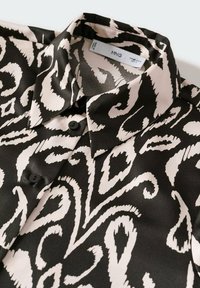 Blusa a fantasia nera e crema con una texture lucida, dotata di un colletto a punta, chiusura con bottoni e design astratti a spirale.