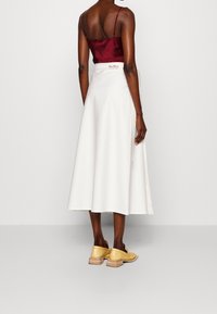 Rode satijnen hemdje gecombineerd met een witte, enkellange rok, voorzien van een strikdetail. Het model draagt gele leren schoenen met een houten hak.