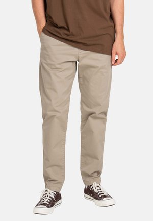 Beige chinos with a straight-leg cut, made of soft cotton fabric, featuring side pockets and a flat front design. Worn with brown sneakers.
