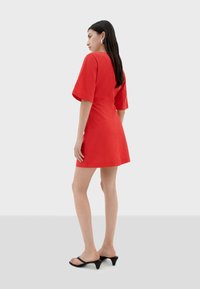 Vestido rojo de manga corta con un cuerpo ajustado y falda acampanada. Confeccionado en una tela suave, presenta un escote redondo y una silueta elegante. Sandalias de tacón negras.