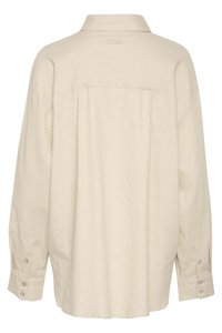 Chemise beige à manches longues en tissu léger, avec un col, des poignets boutonnés et un subtil détail de logo au dos.
