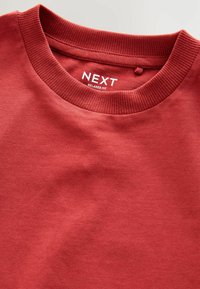 Sweatshirt rouge à col rond avec un col côtelé, texture douce, et étiquette "NEXT RELAXED FIT" bien visible à l'intérieur.