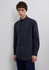 Camisa de manga larga color azul marino con patrón de cuadros, cuello abotonado y botones marrones. Tela suave con un ajuste regular.