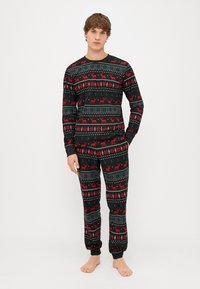 Black pajama set featuring a festive pattern with red reindeer and snowflakes, made of soft fabric, with ribbed cuffs at wrists and ankles.
