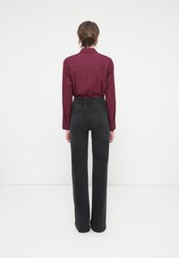 Camisa de manga larga burdeos combinada con jeans negros de cintura alta. La camisa tiene puños con botones; los jeans presentan un diseño de pierna recta y bolsillos.