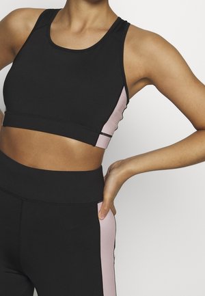 Black sports bra with a pink side panel, featuring a fitted design, smooth texture, and wide straps. Paired with matching high-waisted leggings.