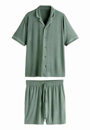 Mann trägt grünes, kurzärmeliges Hemd mit weißen Ziernähten, sichtbar vom Hals bis zur Mitte des Oberkörpers vor neutralem Hintergrund.