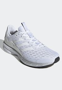 Zapatilla deportiva blanca hecha de malla transpirable, con un diseño bajo y con cordones, parte superior texturizada y suela de goma para mayor agarre.
