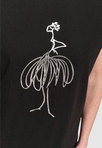 Dibujo abstracto en línea plateada de un pájaro con cabeza parecida a una flor y cola elaborada sobre un fondo de tela negra.