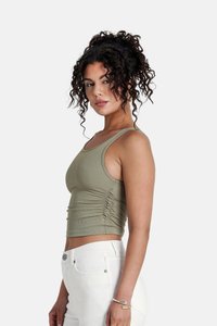 Olijfgroen geribbelde crop top met verstelbare zijkant ruching, dunne banden en een getailleerd silhouet, gecombineerd met witte high-waisted broek.