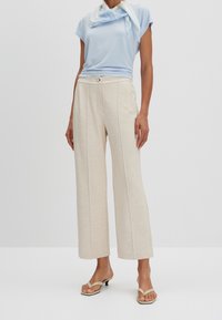 Top de manga corta azul claro combinado con pantalones beige de pierna ancha, que presentan una textura sutil y costuras verticales, complementados con sandalias de tacón nude.