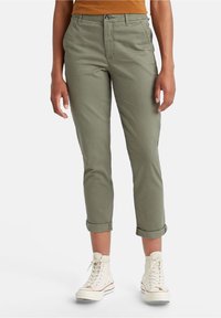 Ljus olivgrön bomullsblandning byxor med uppvikta fållar, frontfickor och dragkedja, matchade med vita högskaftade sneakers.