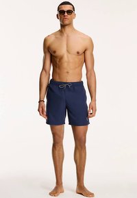 Marineblauwe zwembroek met een elastische tailleband en trekkoord, voorzien van een logopatch aan de zijkant, gemaakt van lichtgewicht stof.