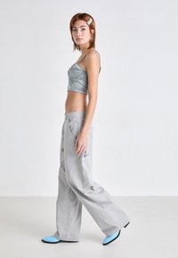 Top corto metálico azul claro, pantalones cargo de pierna ancha gris con bolsillos laterales, y bailarinas azules de punta, lucidos por una modelo de perfil.