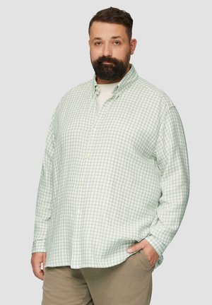 Groen en witte geblokte blouse met geknoopte kraag, lange mouwen en een ontspannen pasvorm, gedragen over een lichtgekleurde t-shirt.