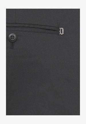 Primo piano di tessuto nero con un piccolo bottone con la scritta "Dondup" e il bordo di una tasca cucita con un ciondolo in metallo a forma di lettera "D".