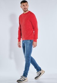 Red ribbed sweater with long sleeves, paired with blue slim-fit jeans and gray-accented sneakers. Simple, clean lines and casual design.