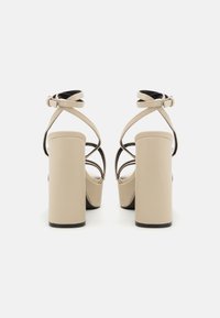 Μπεζ ψηλοτάκουνα σανδάλια με χοντρό κομμάτι τακούνι, πίσω λουράκι και λουράκια που διασταυρώνονται στον αστράγαλο. Λείο φινίρισμα με ελάχιστες λεπτομέρειες.
