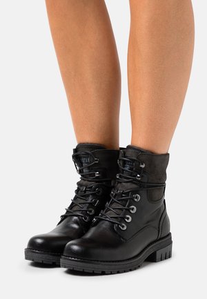 Black leather ankle boots with a suede cuff, round toe, lace-up front, metal eyelets, and textured rubber sole.