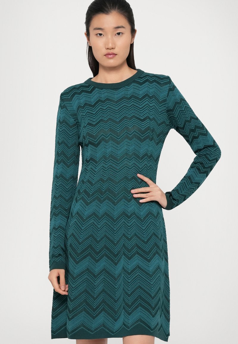Robe en tricot bleu canard avec un motif en zigzag, dotée de longues manches et d'un col rond, fabriquée à partir d'un tissu texturé.
