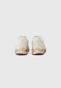 Hvite sneakers med en teksturert overdel og skinnende beige mellomsåle. Har et unikt såledesign og subtil merkevare på baksiden. Gummisåle.