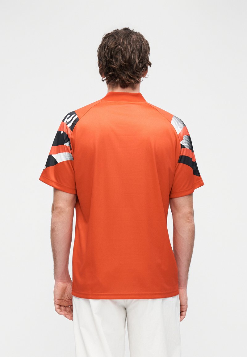Polo orange à manches courtes, avec des accents à motifs noir et blanc sur les épaules. Tissu doux avec un col classique et une coupe décontractée.