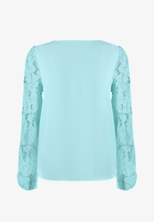 Un chemisier bleu sarcelle clair avec des manches longues en dentelle, présentant un corps en tissu lisse et des motifs délicats de dentelle florale sur les manches.