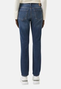 Tmavě modré džíny se slim fit, s dvěma zadními kapsami a značkovým knoflíkem v pase, v kombinaci s bílými teniskami.